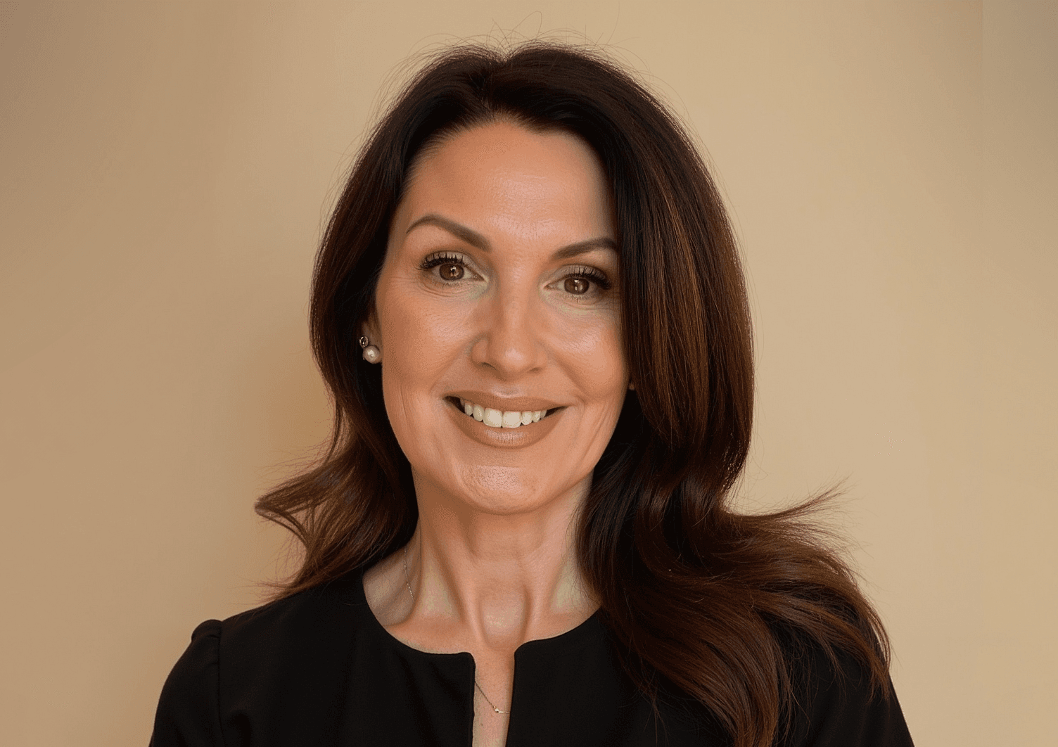 Smiling woman with long dark hair and brown eyes against a neutral tan background.